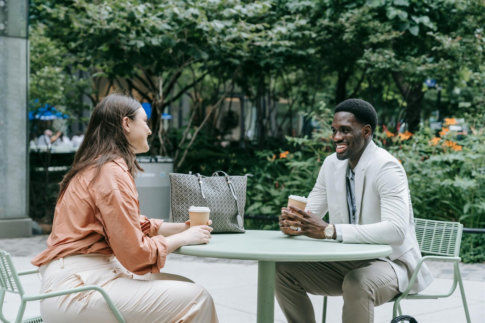 Conversation tenue entre deux personnes à une table de café en extérieur, illustration de la philosophie d'écoute prolongée d'Agent Fédérateur avant toute production de communication