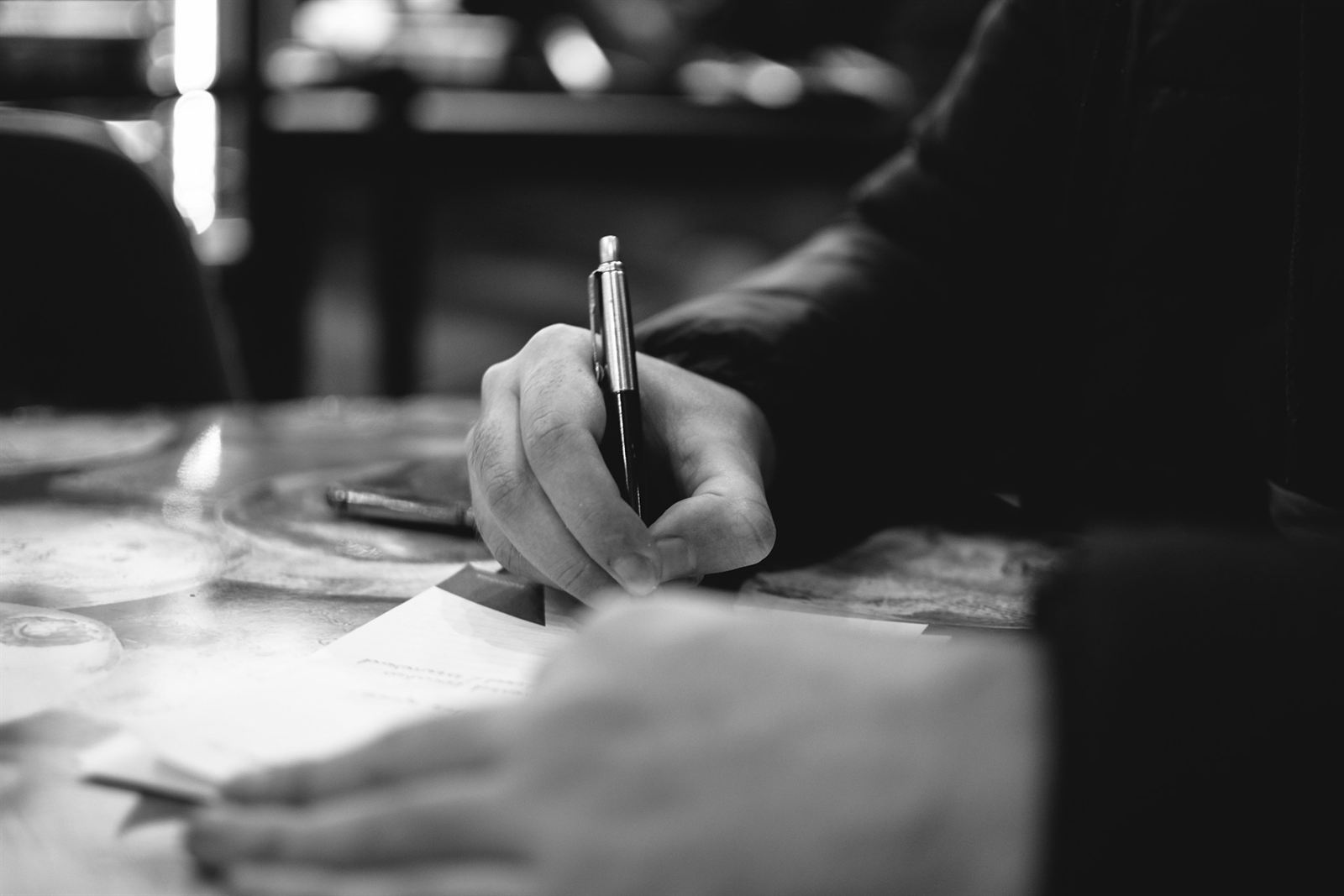 Main qui écrit au stylo sur papier dans une lumière éditoriale tamisée, illustration de la rédaction SEO et de la stratégie de communication qui restent un geste humain
