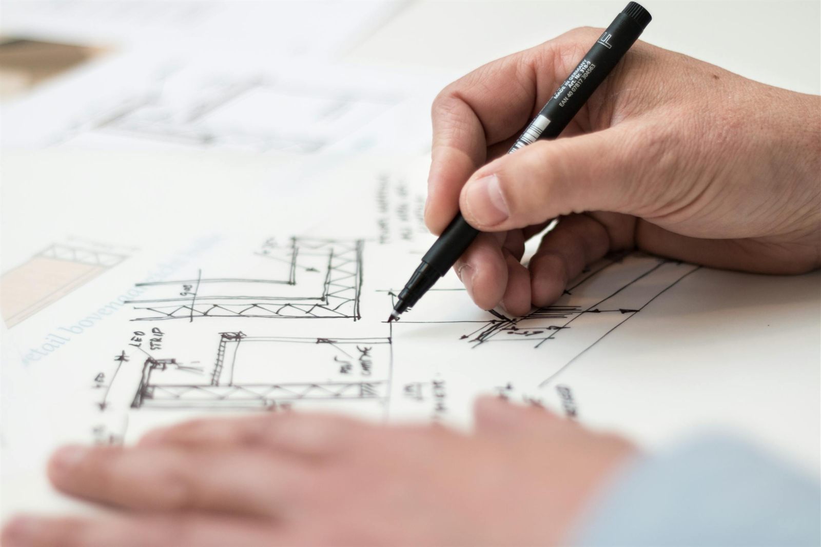 Main dessinant un plan d'architecte technique au stylo sur papier, métaphore de la refonte éditoriale d'un site web : restructurer la pensée avant de construire l'interface