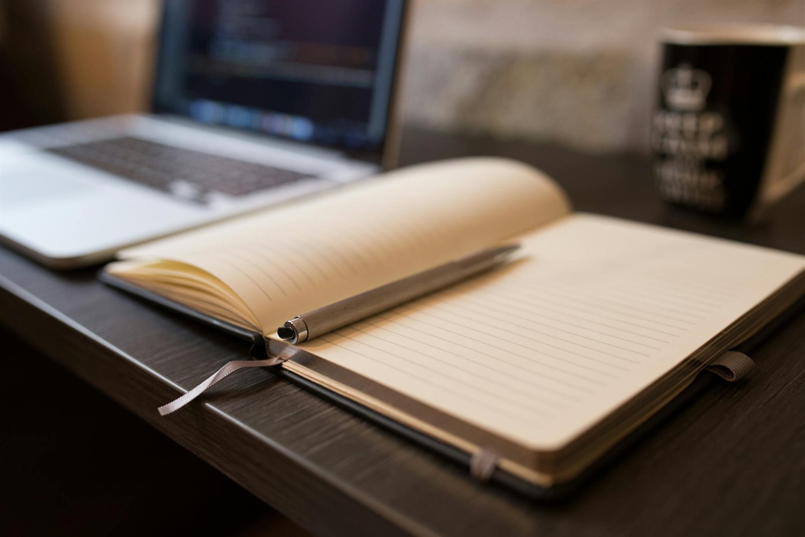 Cahier papier ouvert avec stylo à côté d'un ordinateur portable MacBook sur bureau en bois clair, illustration du rapport critique de Charles Clèdes-Flahaut à l'intelligence artificielle : l'IA accélère, l'humain arbitre